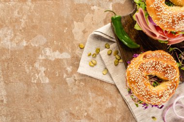 top view of fresh delicious bagels on wooden cutting board on napkin with pumpkin seeds on aged beige surface clipart