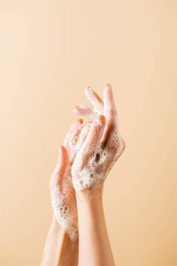 cropped view of female hands in soap foam isolated on beige clipart