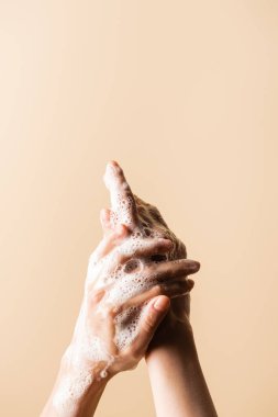 Bej üzerine izole edilmiş sabun köpüğüyle ellerini yıkayan kadının kısmi görüntüsü