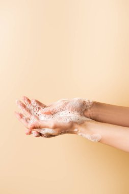 cropped view of female hands in soap foam isolated on beige clipart