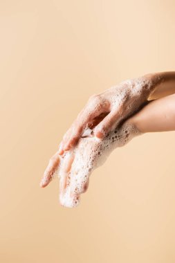 Kırpılmış bej üzerine izole edilmiş sabun köpüğüyle ellerini yıkayan kadın görüntüsü