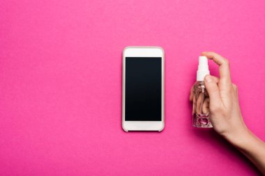 Akıllı telefona antiseptik sıkan bir kadının pembe üzerine beyaz ekran sıktığı kısmen görülüyor.