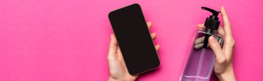 Kadının elinde dezenfektan ve akıllı telefon olan pembe panoramik bir ekran görüntüsü var.