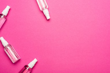 Pembe üzerinde sıvı dezenfektan bulunan saydam sprey şişelerinin üst görüntüsü