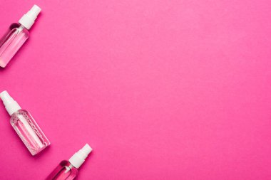 Pembe üzerinde el dezenfektanı olan saydam sprey şişelerinin üst görüntüsü