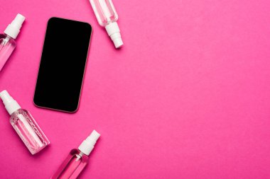 Pembe ekranı boş olan akıllı telefonun yanında dezenfektanla saydam sprey şişelerin üst görüntüsü