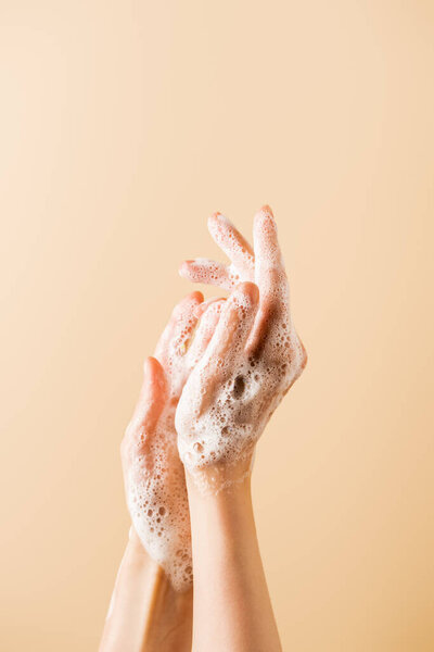 cropped view of female hands in soap foam isolated on beige