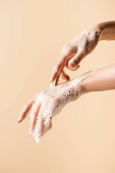 partial view of female hands in soap foam isolated on beige