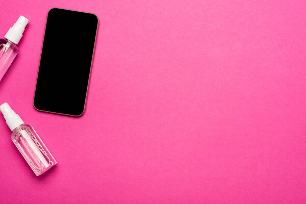 вид сверху на бутылки с дезинфицирующими средствами рядом со смартфоном с чистым экраном на розовом

