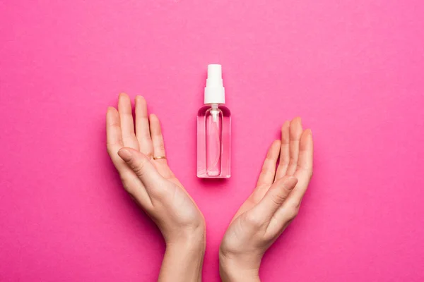 粉红上有手部清洁剂的喷雾瓶附近女性双手的局部透视 — 图库照片