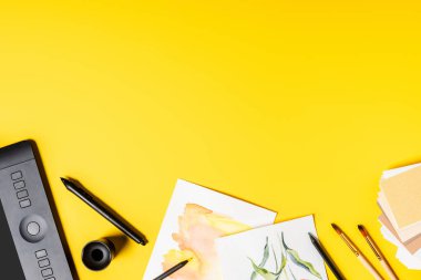Stylus 'un yanında tablet, resim ve boya fırçaları ve sarı kalemlerin üst görünümü