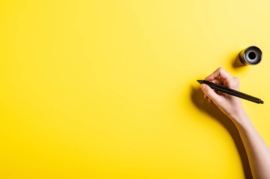 cropped view of designer holding stylus in hand on yellow  clipart