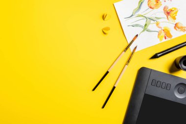 Boyaya yakın boya fırçalarının üst görünümü, kağıt kesiği elementler, sarı üzerine tablet ve stil çizimi 