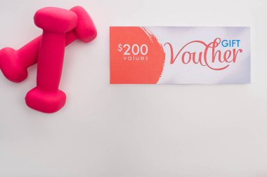 Beyaz arkaplanda 200 dolarlık hediye çeki olan pembe halterlerin üst görünümü