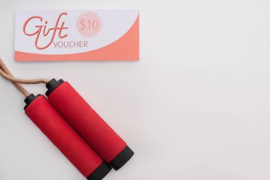 Top view of skipping rope near gift voucher with 10 dollars sign on white background  clipart