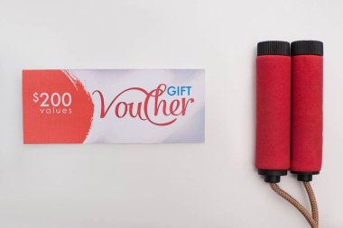 Top view of gift voucher with 200 dollars sign near jump rope on white background clipart
