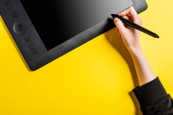cropped view of designer holding modern stylus near drawing tablet with blank screen on yellow 