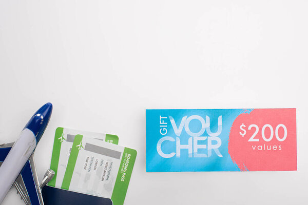 Верхний вид паспорта с посадочными талонами, игрушечным самолетом и подарочным сертификатом с табличкой 200 значений на белом фоне
