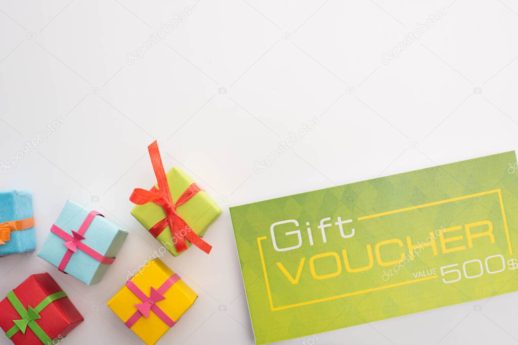 Top view of gift boxes near green gift voucher on white background