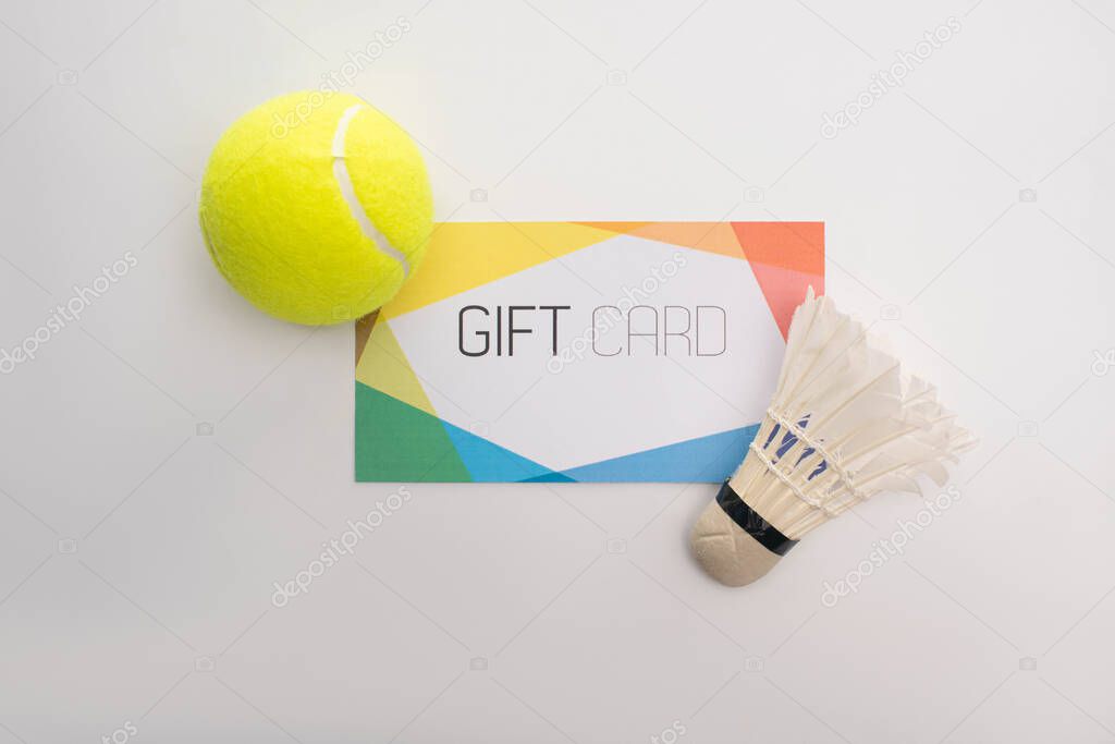 Top view of gift card near tennis ball and shuttlecock on white surface
