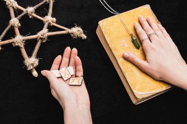 Cadı rünlerini tutarken üst görünüm ve siyah üzerinde pentagram yanında eski kitap koymak