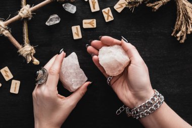 top view of witch holding crystals near runes on black  clipart