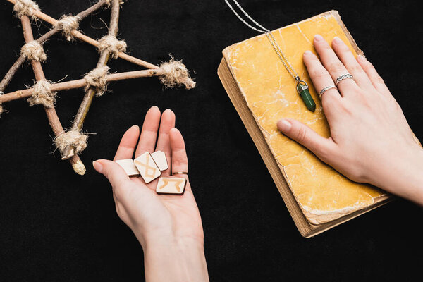 верхний вид ведьма держит руны и положить руку на старую книгу около пентаграммы на черный
