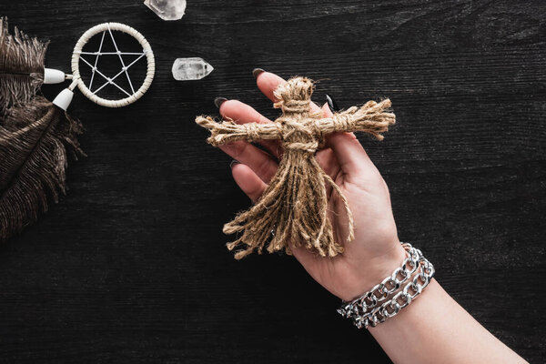 top view of woman holding voodoo doll near pentagram and crystals on black 