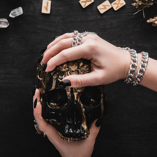 close up of woman holding skull near runes and crystals on black 