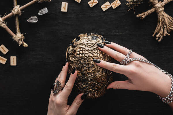 top view of woman touching skull near runes, voodoo doll and crystals on black 