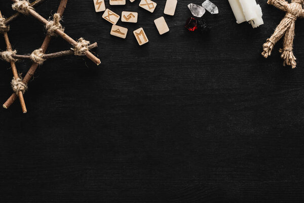 top view of runes, pentagram, candles, crystals and voodoo doll on black