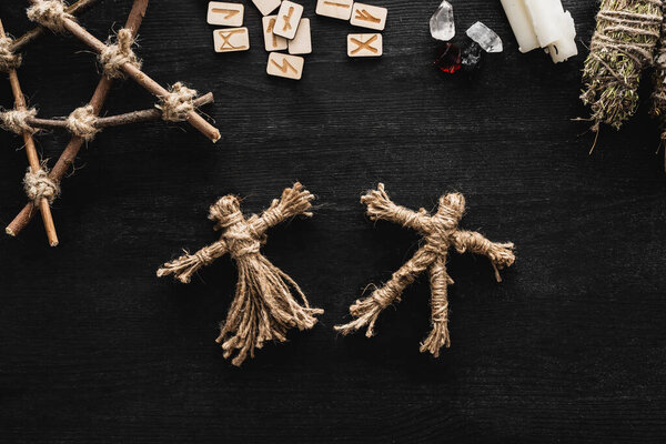 top view of voodoo dolls, scandinavian runes, pentagram, candles and crystals on black