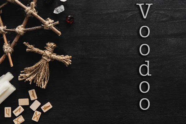 top view of voodoo dolls, ancient runes, pentagram, candles and crystals near voodoo lettering on black