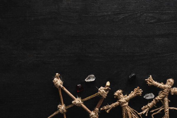 top view of voodoo dolls, ancient crystals and pentagram on black