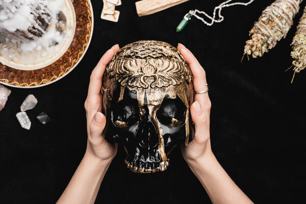 верхний вид ведьмы, держащей череп возле рун, свечей и кристаллов на черном
 