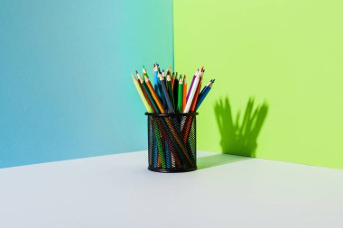Mavi, yeşil ve beyaz arka planda renkli kalemleri olan kalem tutucu