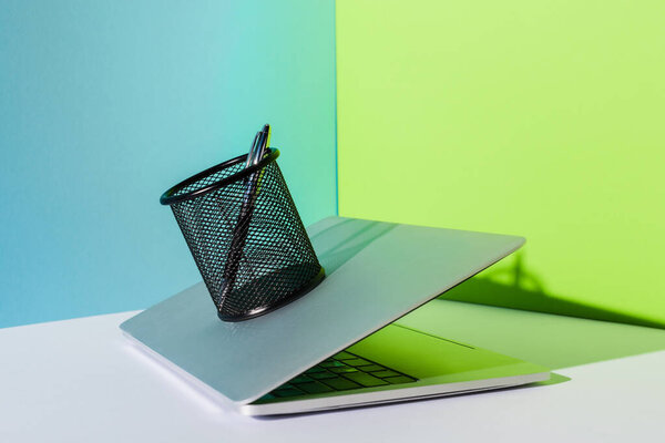 pen in holder on modern laptop on blue, white and green background
