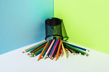 Mavi, yeşil ve beyaz arka planda kalem tutucusundan yayılmış renkli kalemler
