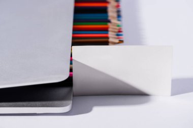 Boş kartvizitlerin ve renkli kalemlerin modern dizüstü bilgisayarlarda beyaz arka planda seçici odak noktası