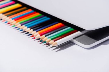 Modern dizüstü bilgisayardaki renkli kalemlerin beyaz arkaplandaki görüntüsünü kapat