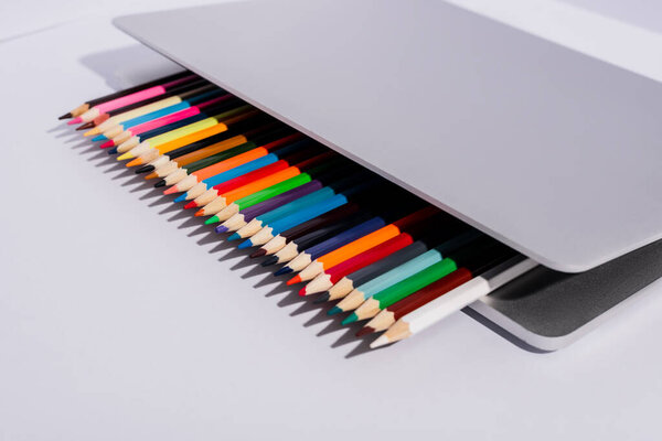цветные карандаши в современном ноутбуке на белом фоне
