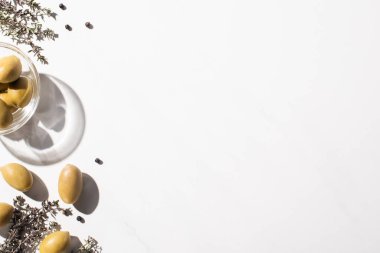 Kasede yeşil zeytin, otlar ve beyaz arka planda siyah biber manzarası.