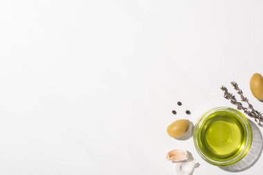 Yeşil zeytinlerin, sarımsağın, otun ve beyaz arka planda siyah biberin yanında zeytin yağının üst görüntüsü.