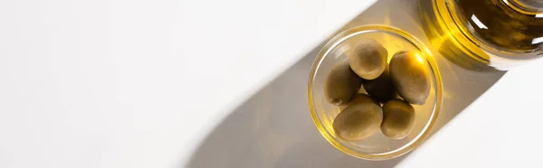 在白色背景阴影下的碗中绿色橄榄附近的瓶子中橄榄油的顶部视图 全景方向 — 图库照片