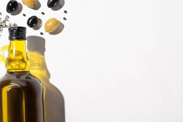 top view of olive oil in bottle near green and black olives and black pepper on white background with shadow