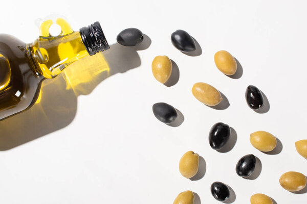 top view of olive oil in bottle near green and black olives on white background with shadow