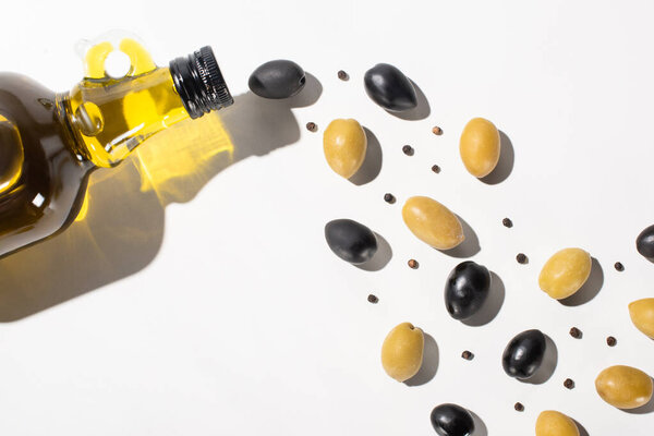 top view of olive oil in bottle near green and black olives and black pepper on white background with shadow