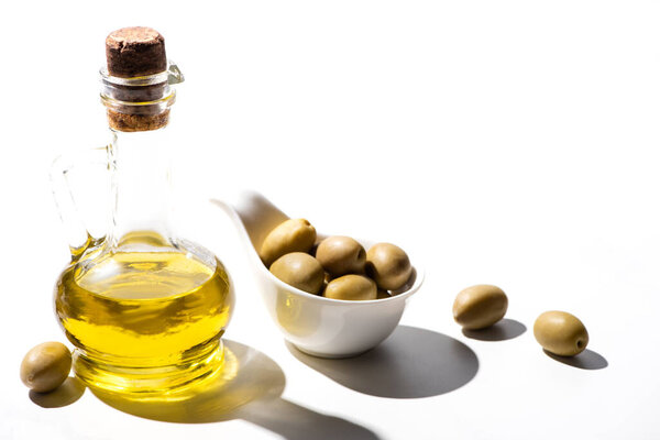 olive oil in jar near green olives in bowl on white background