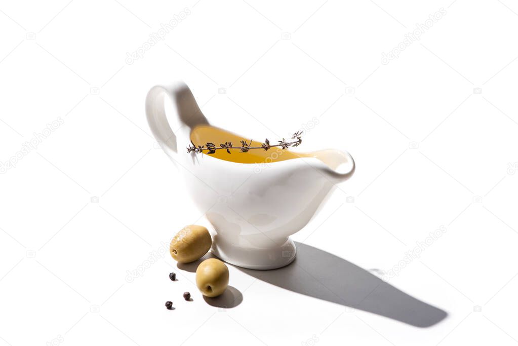 olive oil in sauce boat near green olives and black pepper on white background