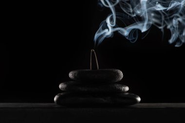 burning incense on stones with smoke on black background clipart